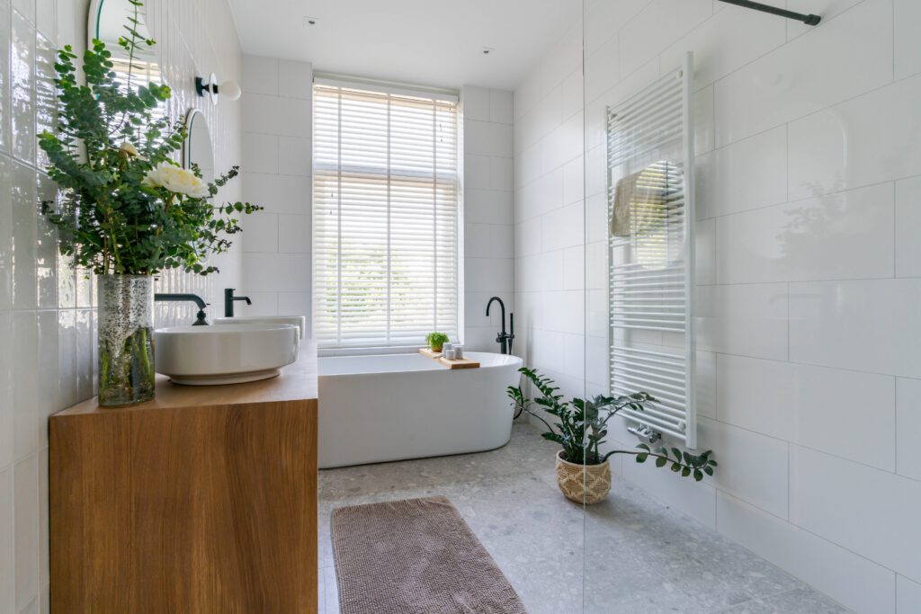 Luxe badkamer met een wit vrijstaand bad en grote kamerplanten voor het raam.