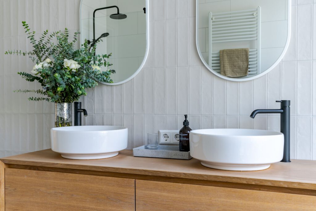 Detail van een badkamer met een ronde spiegel en ingebouwde zwarte wandkraan boven een waskom.